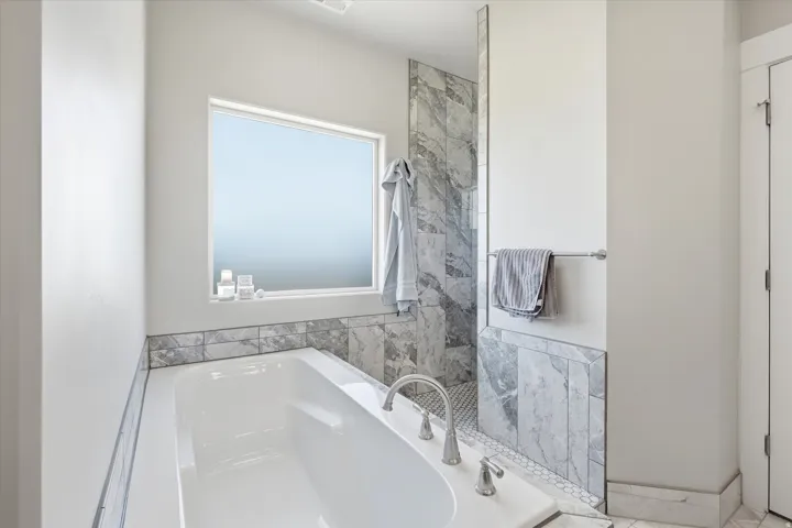 Soaking tub with deck-mounted chrome fixtures, complemented by a window sill, and surrounded by large-format natural stone-look tiles