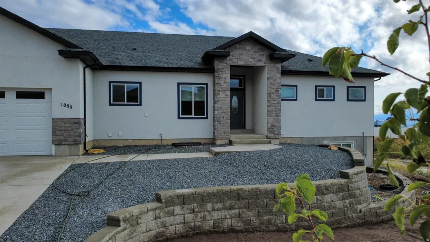 Stucco exterior with stone accenting, dark shingled roof, attached garage, and a retaining wall