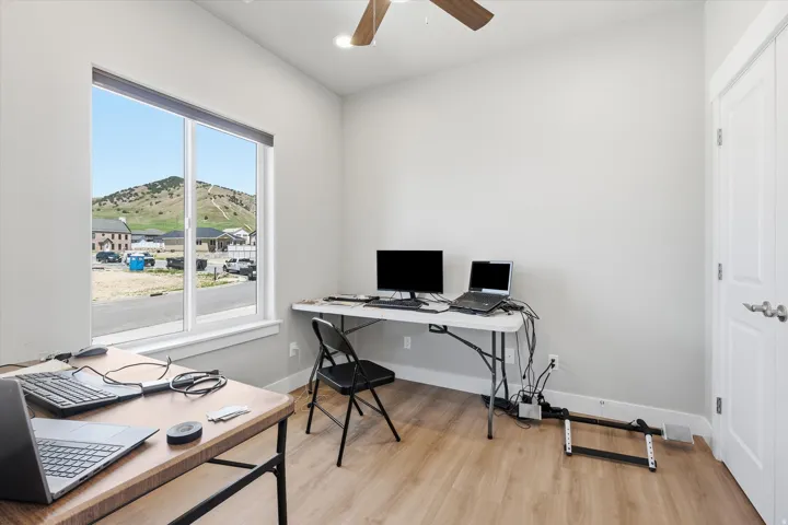 Room featuring wood-finish flooring, a ceiling fan, and a large window with white trim