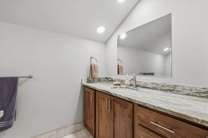 Bathroom vanity featuring a light-toned stone countertop with an integrated sink, wood-finish cabinetry, and a rectangular mirror