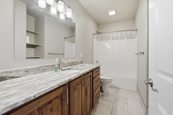 Bathroom featuring a double vanity with wood-finish cabinetry, a light-toned patterned countertop, an integrated sink, and a large mirror with overhead lighting