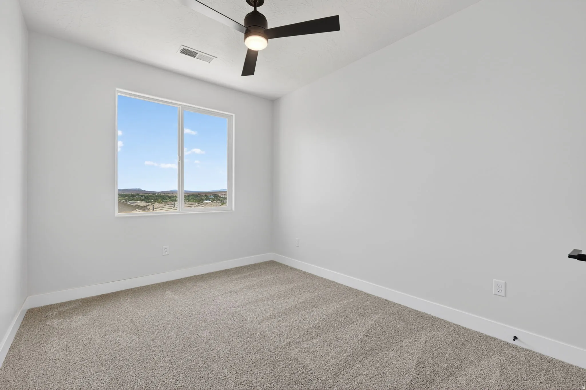 Room featuring a large window, neutral carpeting, white walls, and a black ceiling fan with integrated lighting