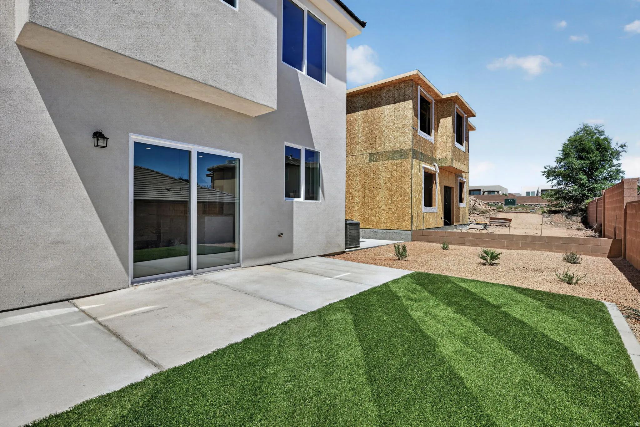 Rear exterior featuring a patio, sliding glass door, and a partially landscaped yard with artificial turf and decorative rock