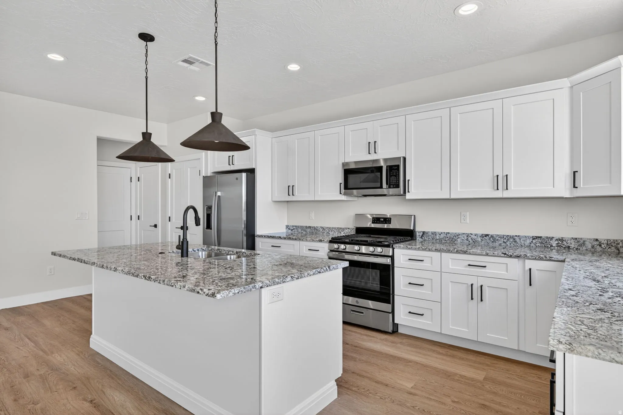 Modern kitchen featuring an island with a built-in sink, white shaker-style cabinetry, granite countertops, and stainless steel appliances