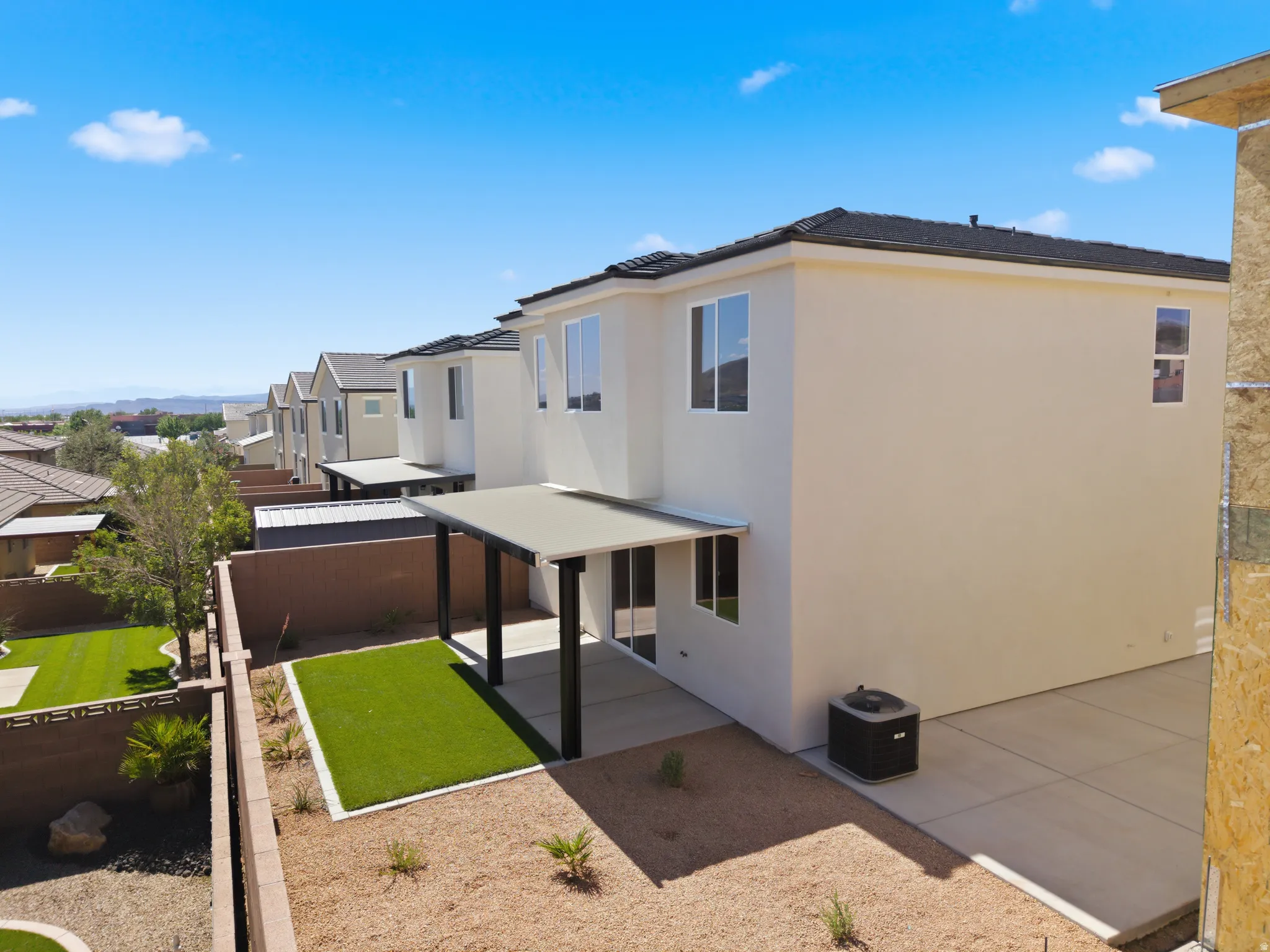Rear exterior featuring a covered patio with direct access to interior spaces, a landscaped yard with artificial turf and gravel, and a concrete patio