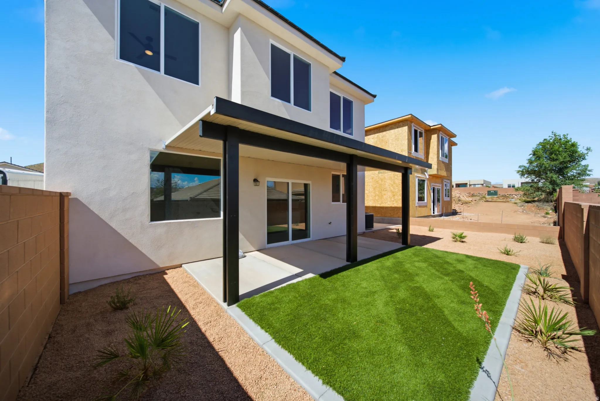 Rear exterior featuring a covered patio, artificial turf area, and desert landscaping