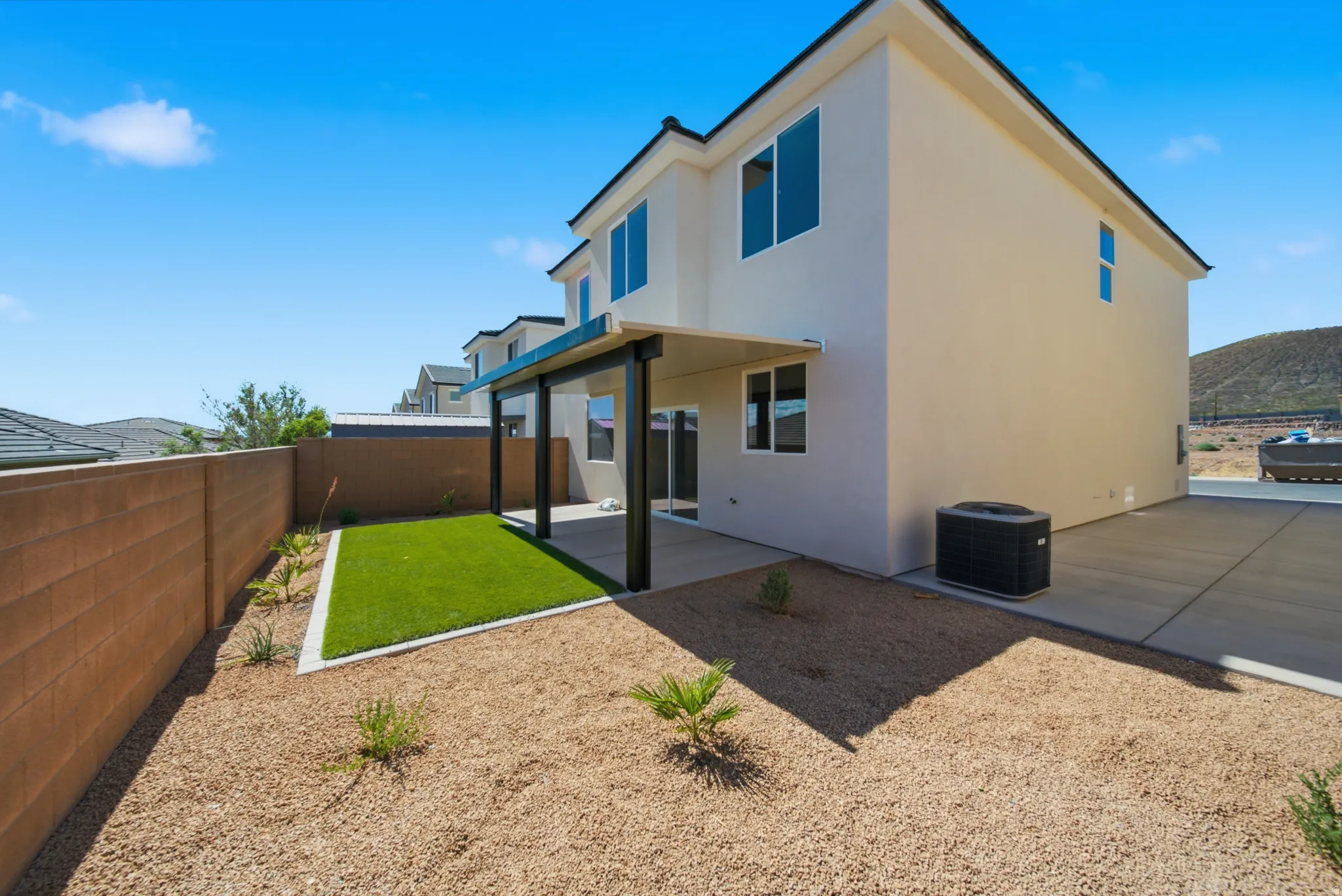 Backyard featuring an extended concrete patio, artificial turf area, and gravel landscaping