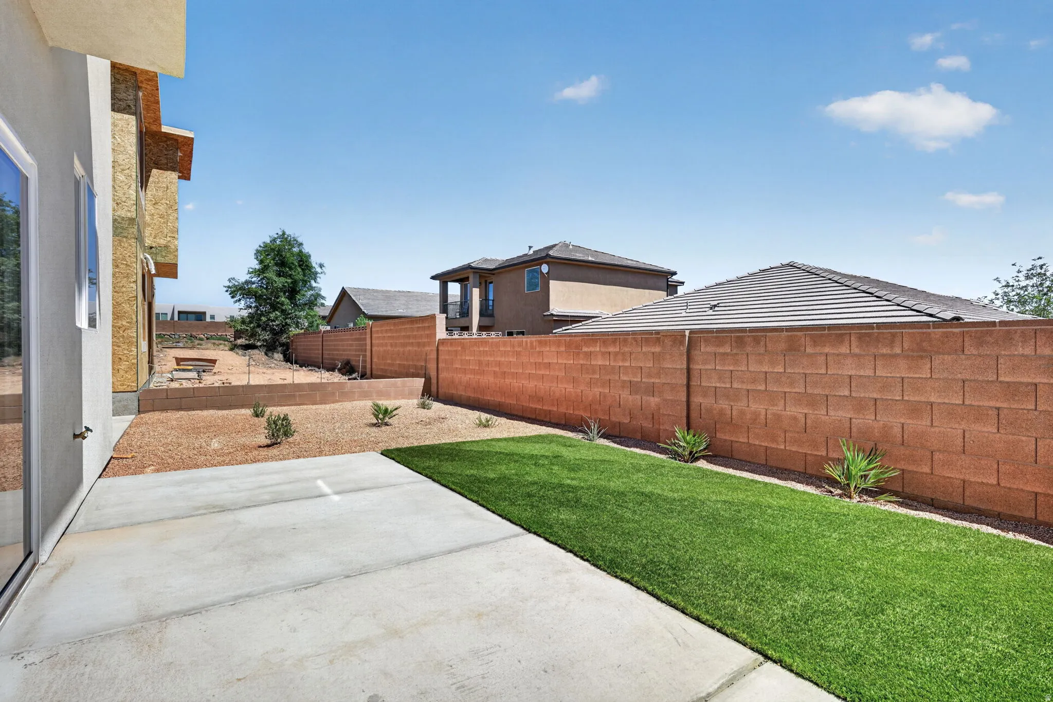 Outdoor patio area featuring a concrete slab, a strip of artificial turf, and a gravel landscape bed