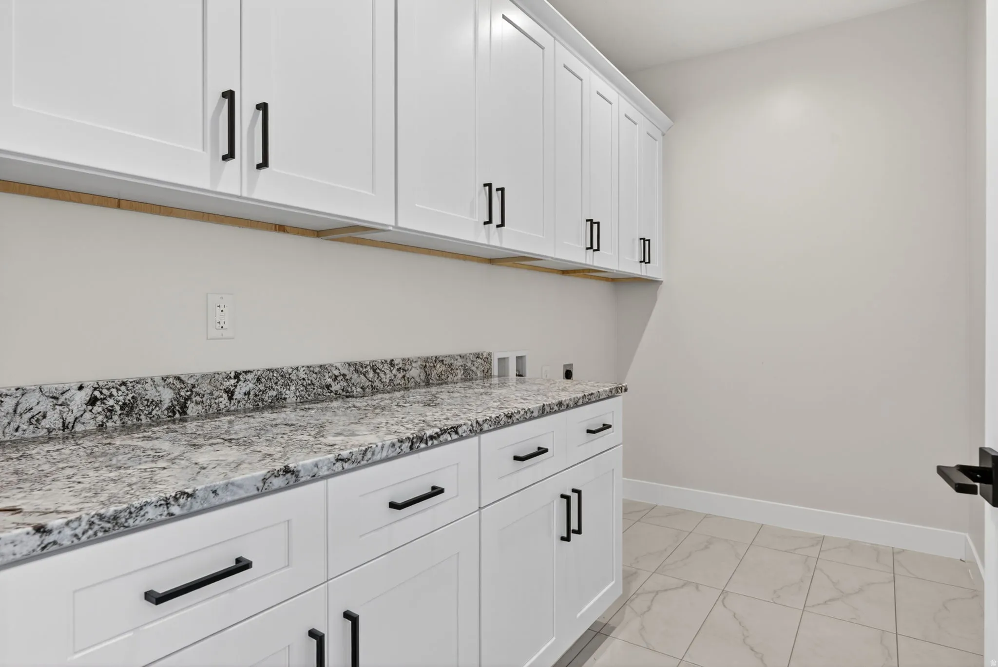 Laundry room featuring extensive white shaker-style cabinetry, granite-patterned countertops, and dark hardware