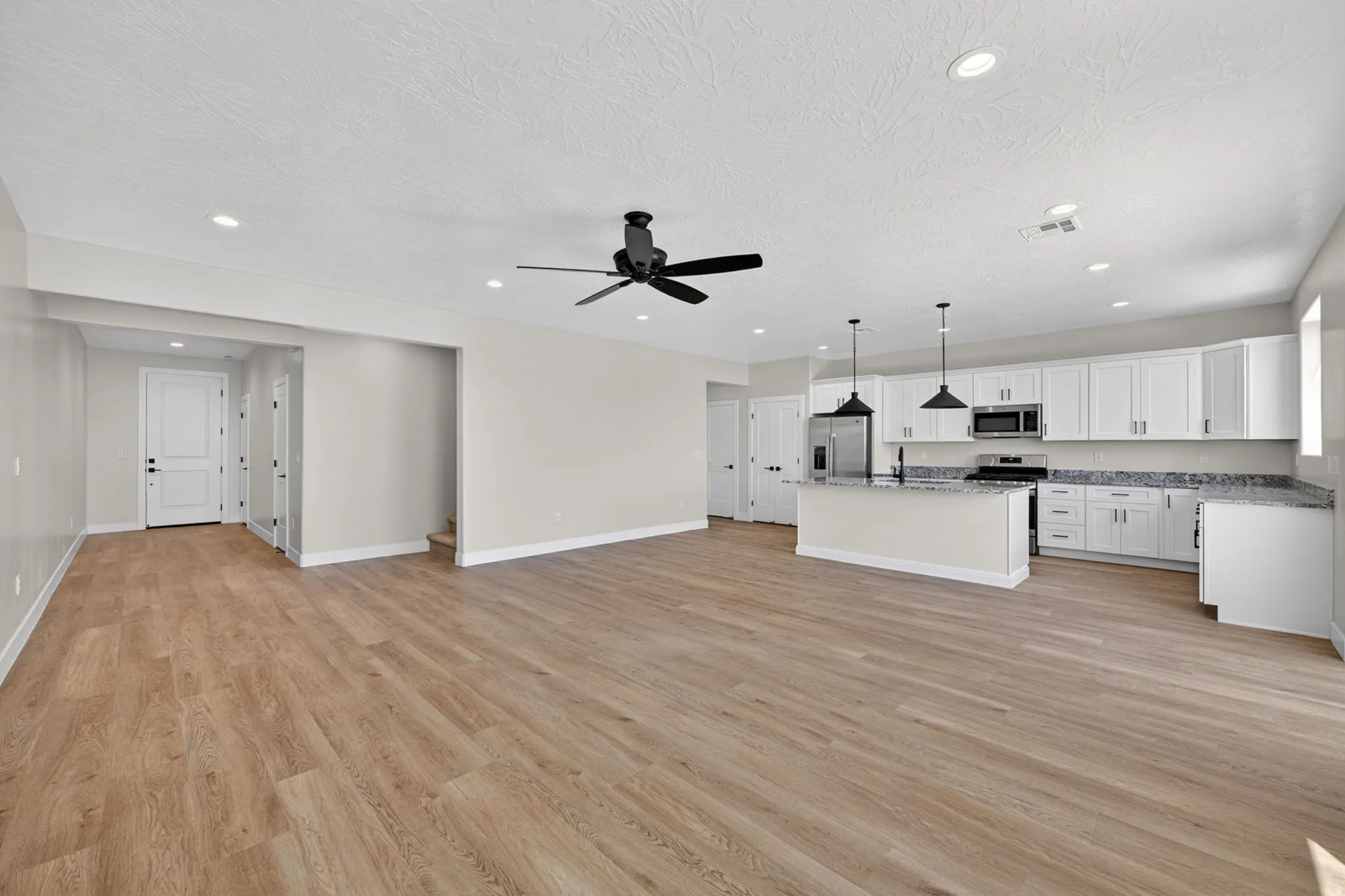 Open-concept living space with wood-finish flooring, recessed lighting, and a contemporary ceiling fan