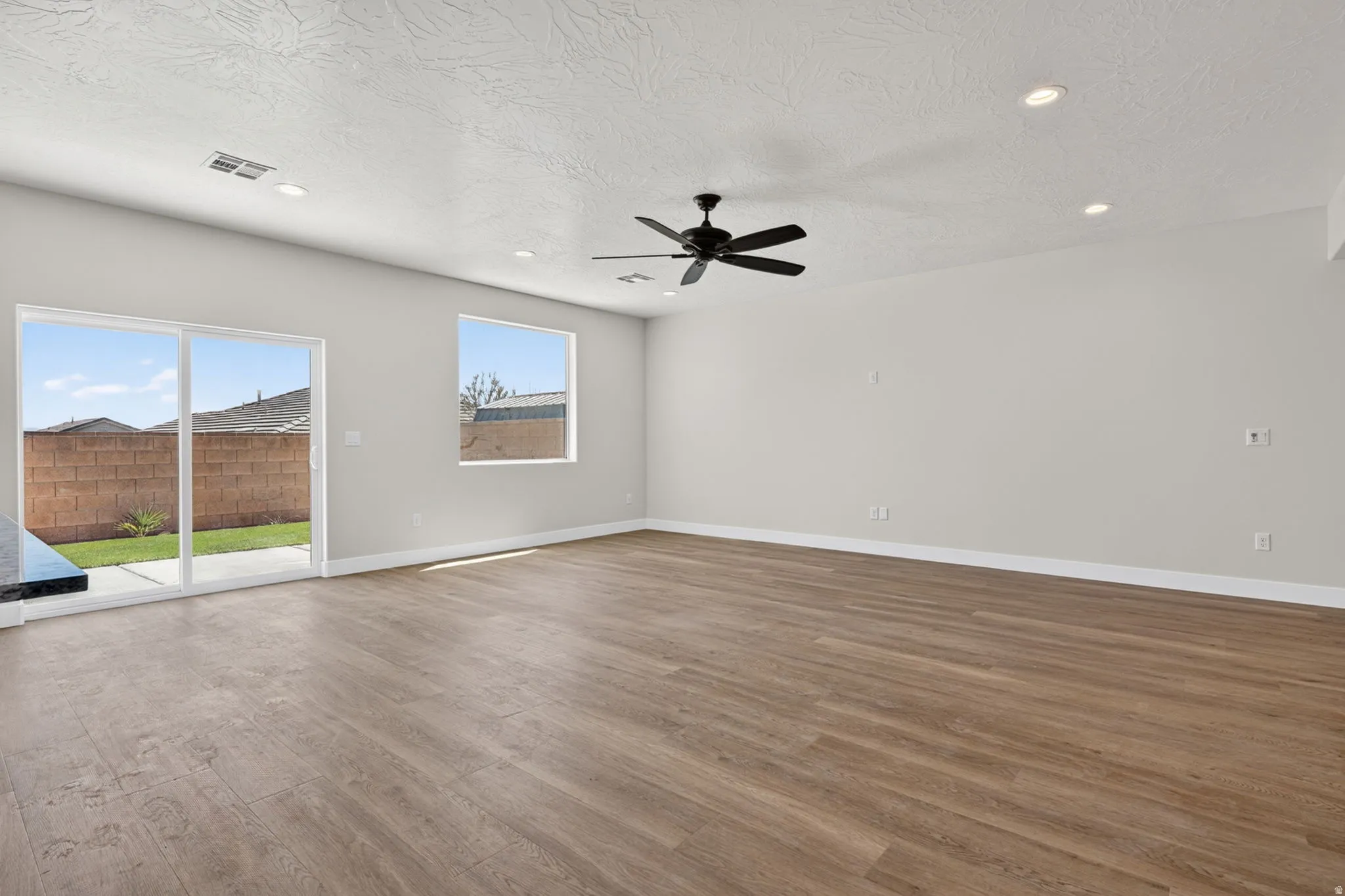 Spacious interior featuring wood-finish flooring, light grey walls, and a multi-speed ceiling fan