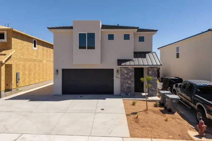 Contemporary exterior featuring a stucco finish, stone accents, dark garage door, and a covered entry