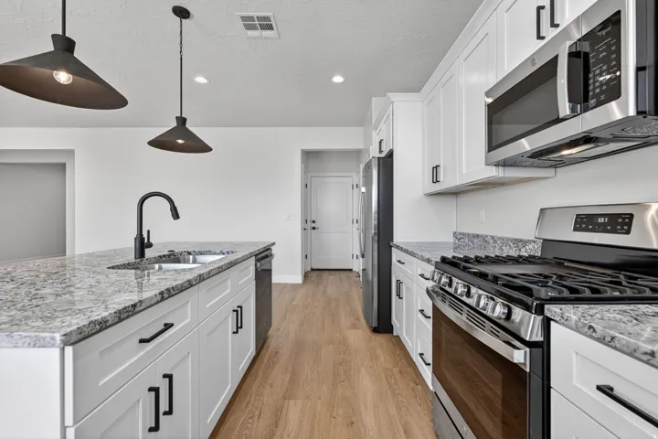 Bright kitchen featuring a central island with an undermount sink and matte black faucet, surrounded by white shaker cabinetry and light granite countertops