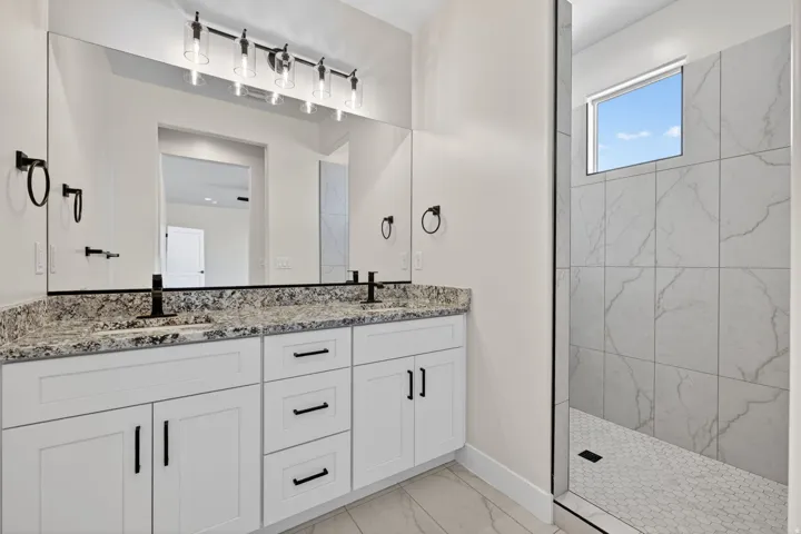 Dual sink vanity featuring a granite countertop with black fixtures and white shaker-style cabinetry