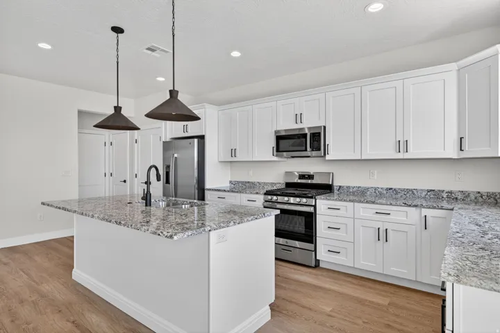 Modern kitchen featuring an island with a built-in sink, white shaker-style cabinetry, granite countertops, and stainless steel appliances