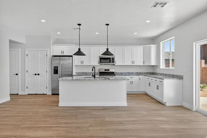 Modern kitchen featuring white cabinetry, granite countertops, a stainless steel appliance suite, and wood-finish flooring