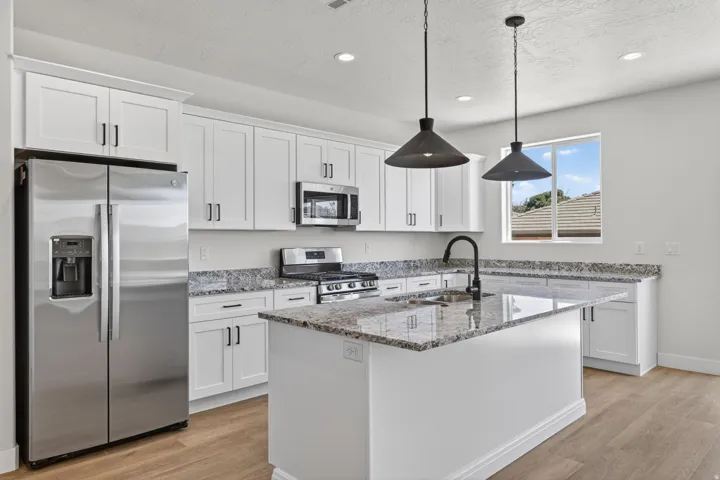 Modern kitchen featuring white shaker cabinetry, stainless steel appliances, a center island with sink, pendant lighting, and wood-finish flooring
