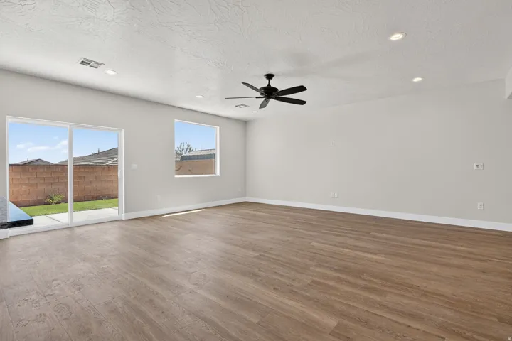 Spacious interior featuring wood-finish flooring, light grey walls, and a multi-speed ceiling fan