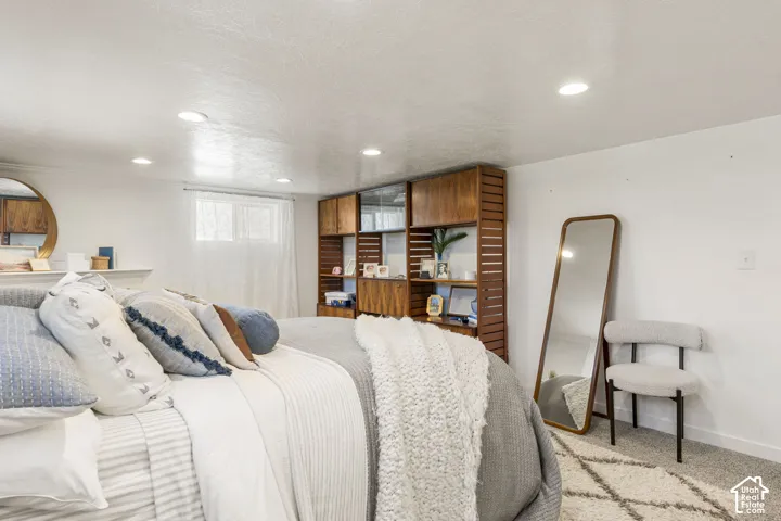 Recessed ceiling lighting illuminates a room featuring a large window with sheer white curtains and light gray wall-to-wall carpeting