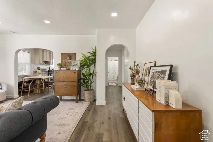 Archway entrances providing access to the kitchen and a hallway, recessed lighting, and wood-finish flooring throughout
