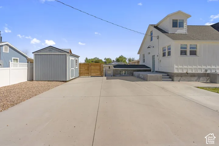 Paved driveway with a detached storage shed, privacy fencing, and exterior lighting