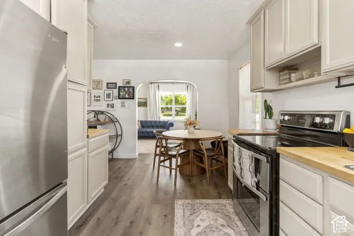 Galley kitchen featuring light-toned cabinetry, wood-finish countertops, stainless steel appliances, and wood-finish flooring