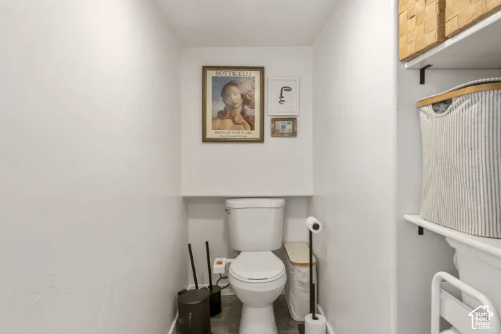 Primary bathroom featuring a white toilet, integrated shelving with black brackets, and light-toned flooring