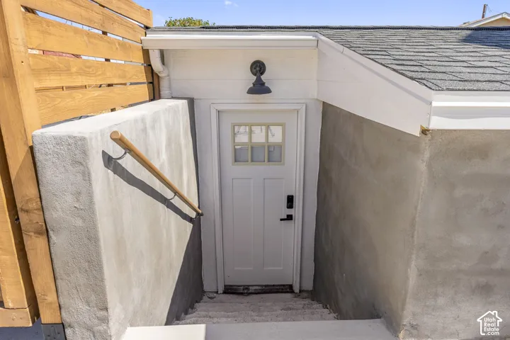 Attached ADU entry featuring a white paneled door with glass inserts, a gooseneck outdoor light fixture, a wood-finish handrail, concrete retaining walls, and wood fencing