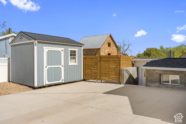 Spacious concrete patio with a light blue storage shed featuring a metal roof and a horizontal slat wood fence