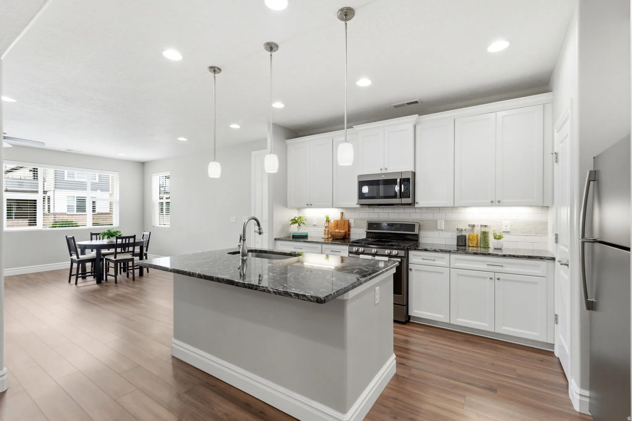 Kitchen featuring white shaker cabinetry, stainless steel appliances, dark stone countertops, and a subway tile backsplash
