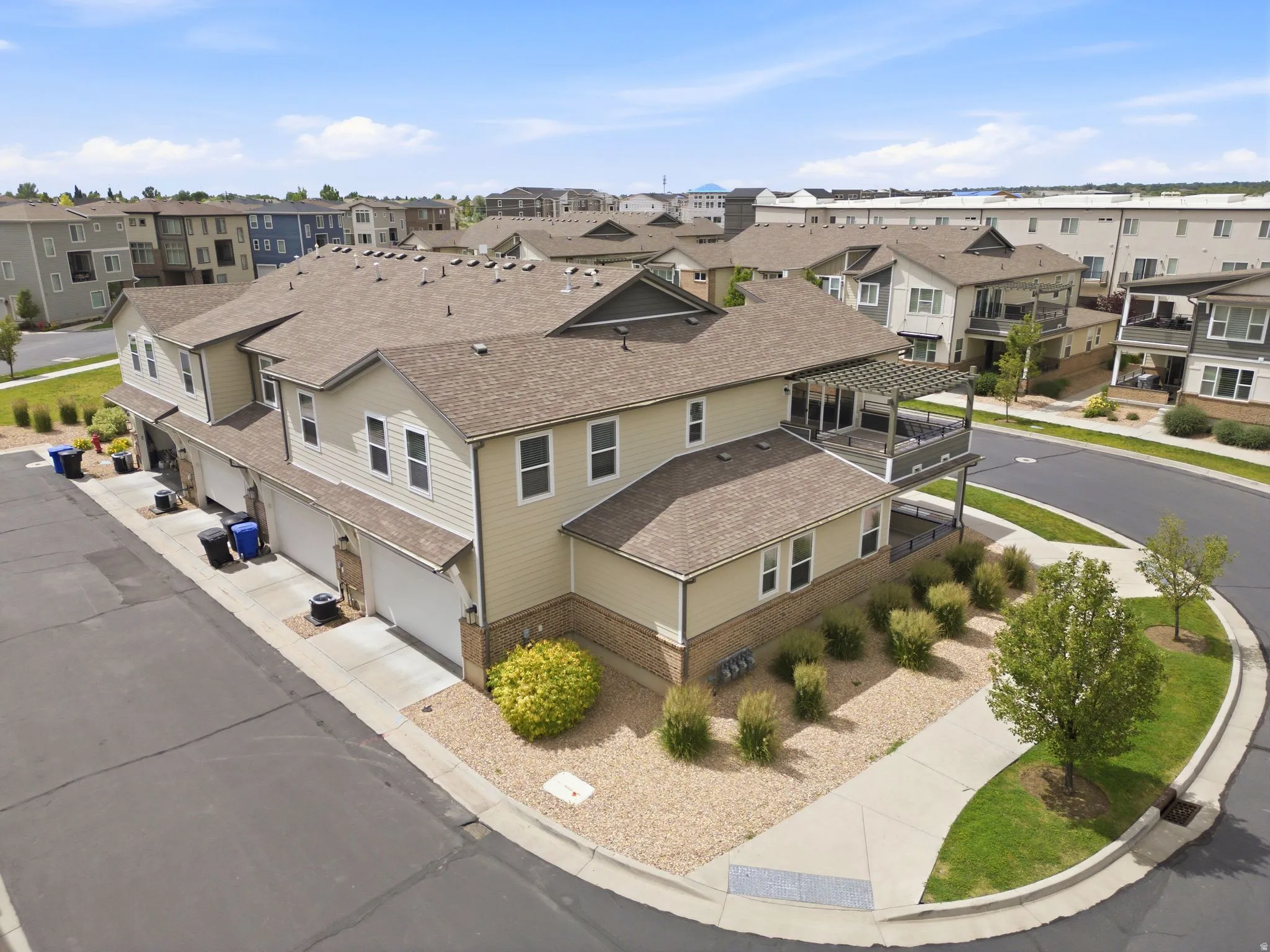 Townhome complex featuring light-colored siding, multiple attached garages, and an upper-level balcony with a pergola