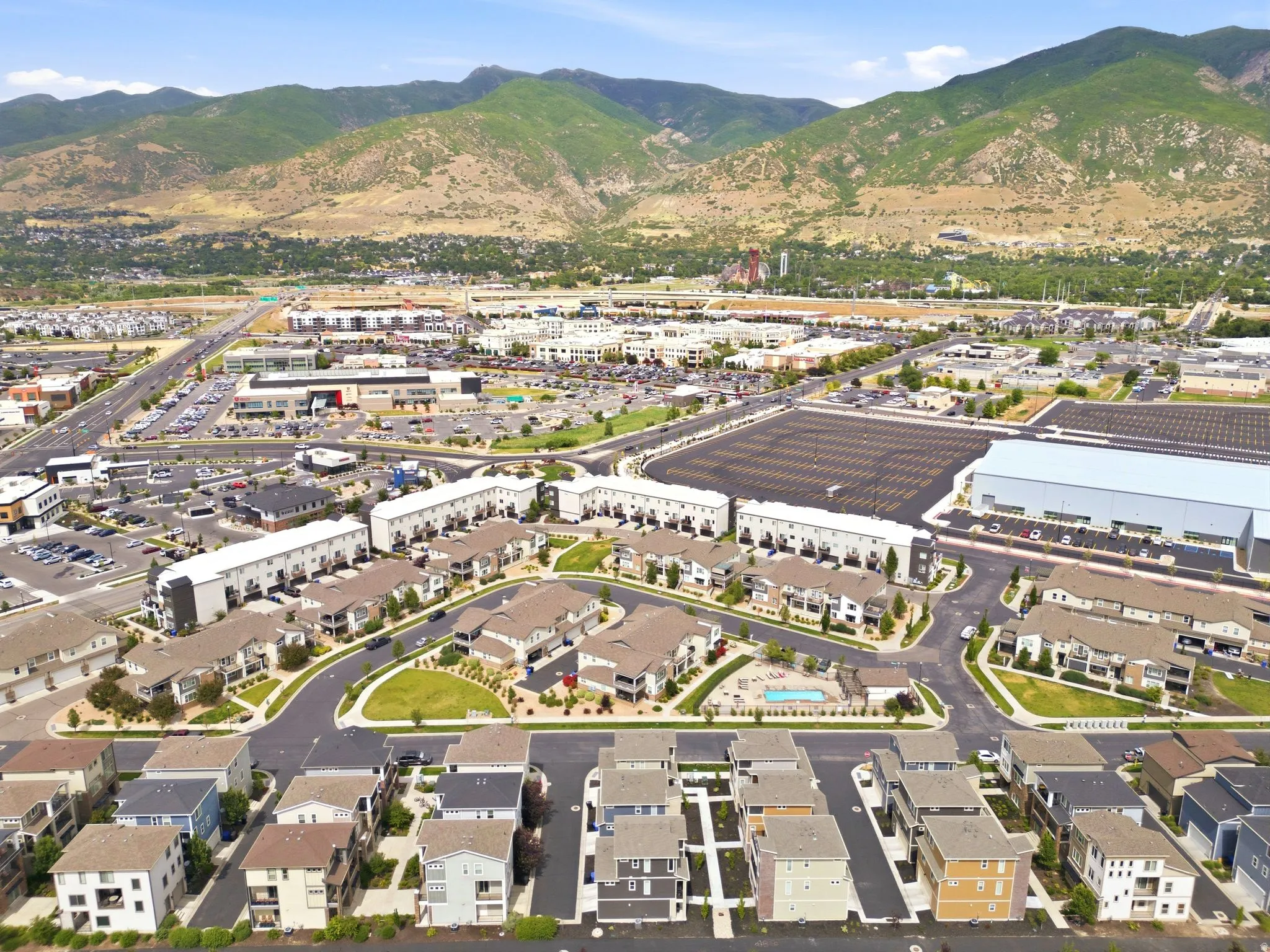 Aerial perspective showcasing a residential development with a community pool, surrounded by commercial establishments and a prominent mountain range backdrop