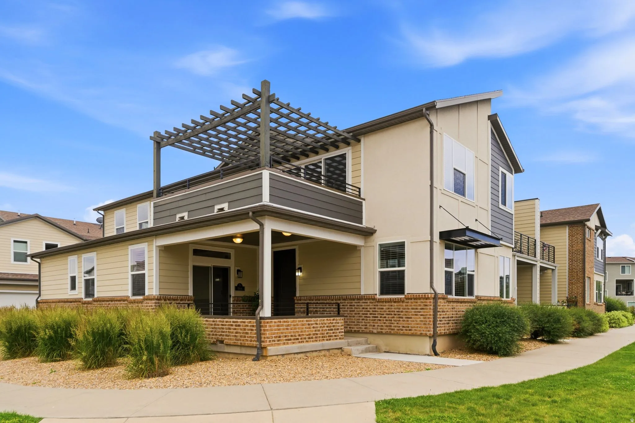 Contemporary multi-level exterior with a pergola-covered upper balcony, covered porch, large windows, and a brick base