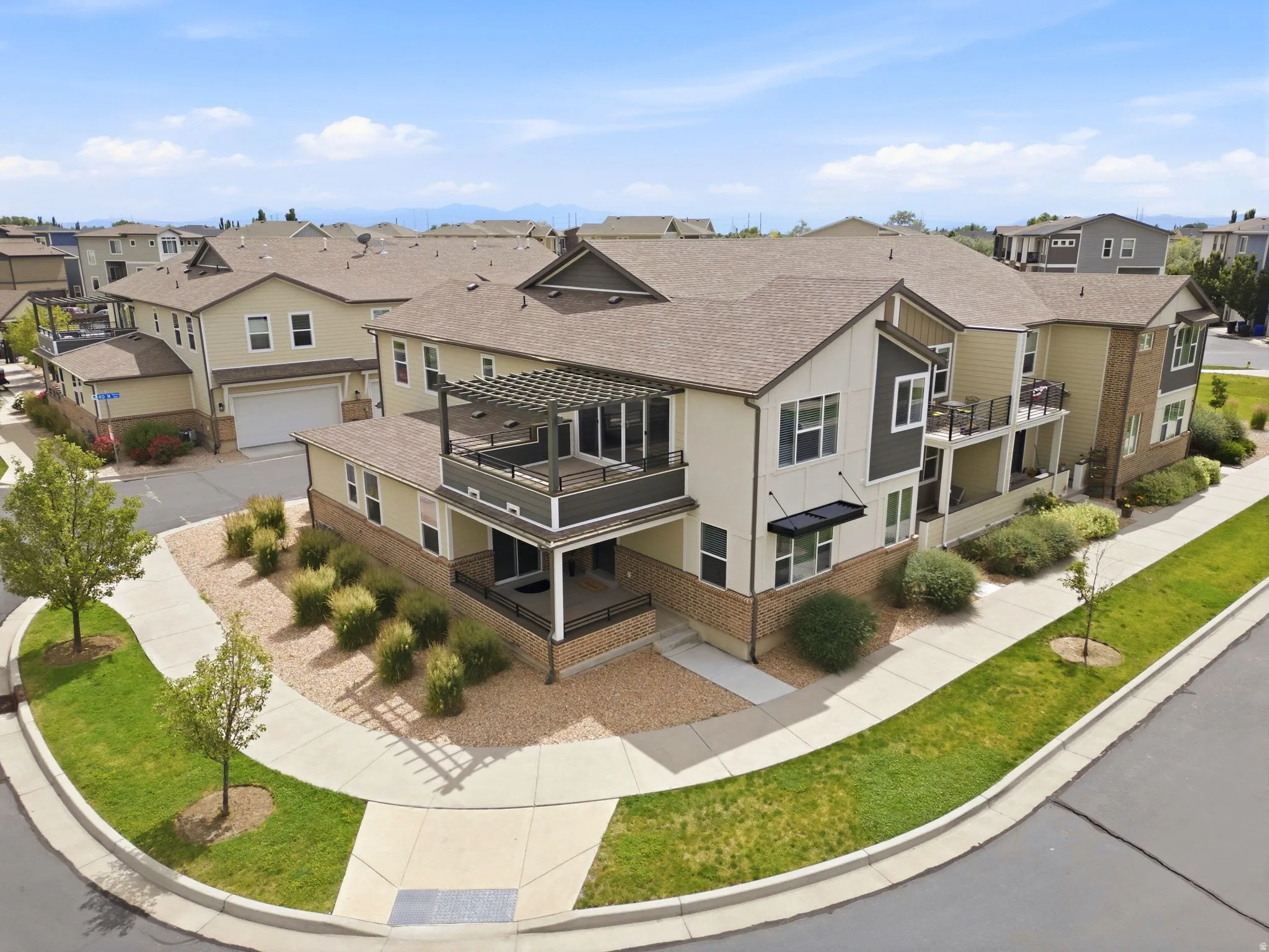 Multi-level townhouse exterior featuring a private balcony with a pergola, ground-level patio, and a two-car garage