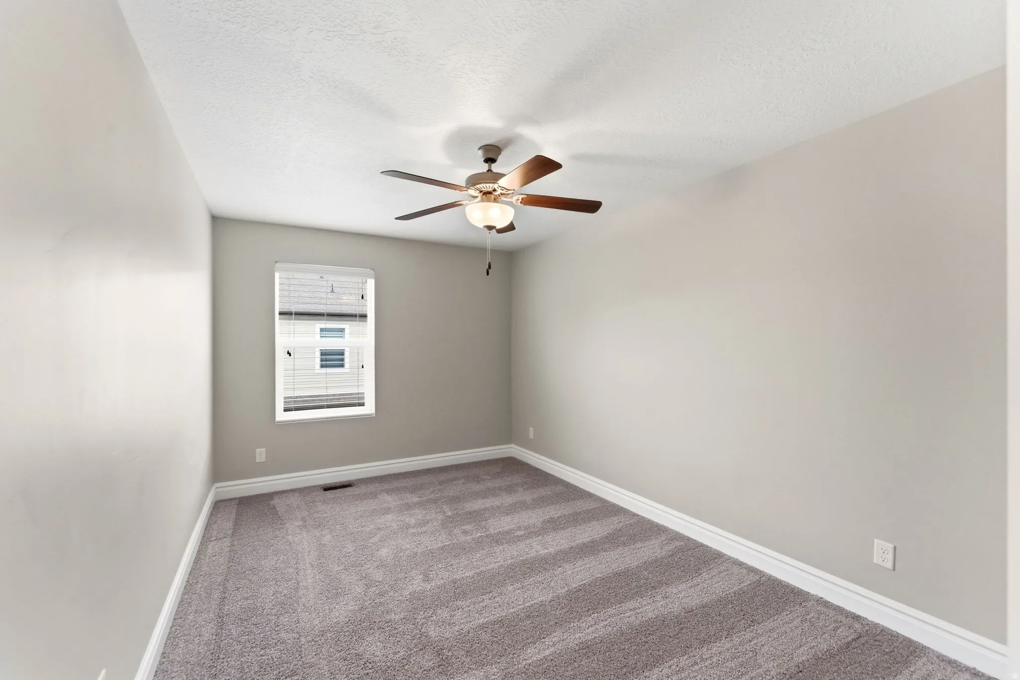 Room featuring light gray walls, textured gray carpeting, white baseboards, and a window with white blinds