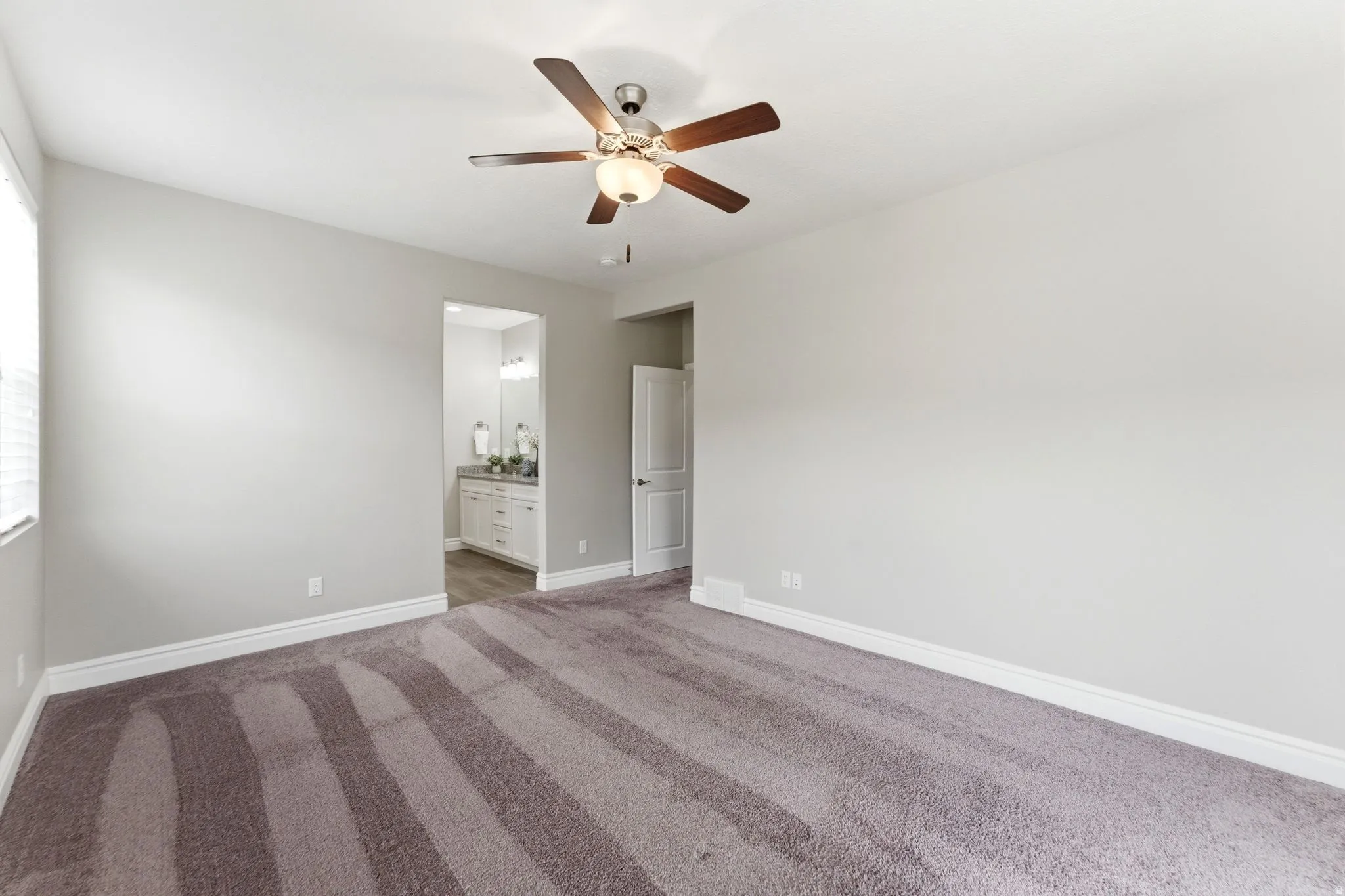 Spacious room featuring neutral-toned walls, plush carpet flooring, a ceiling fan with integrated lighting, and white baseboards
