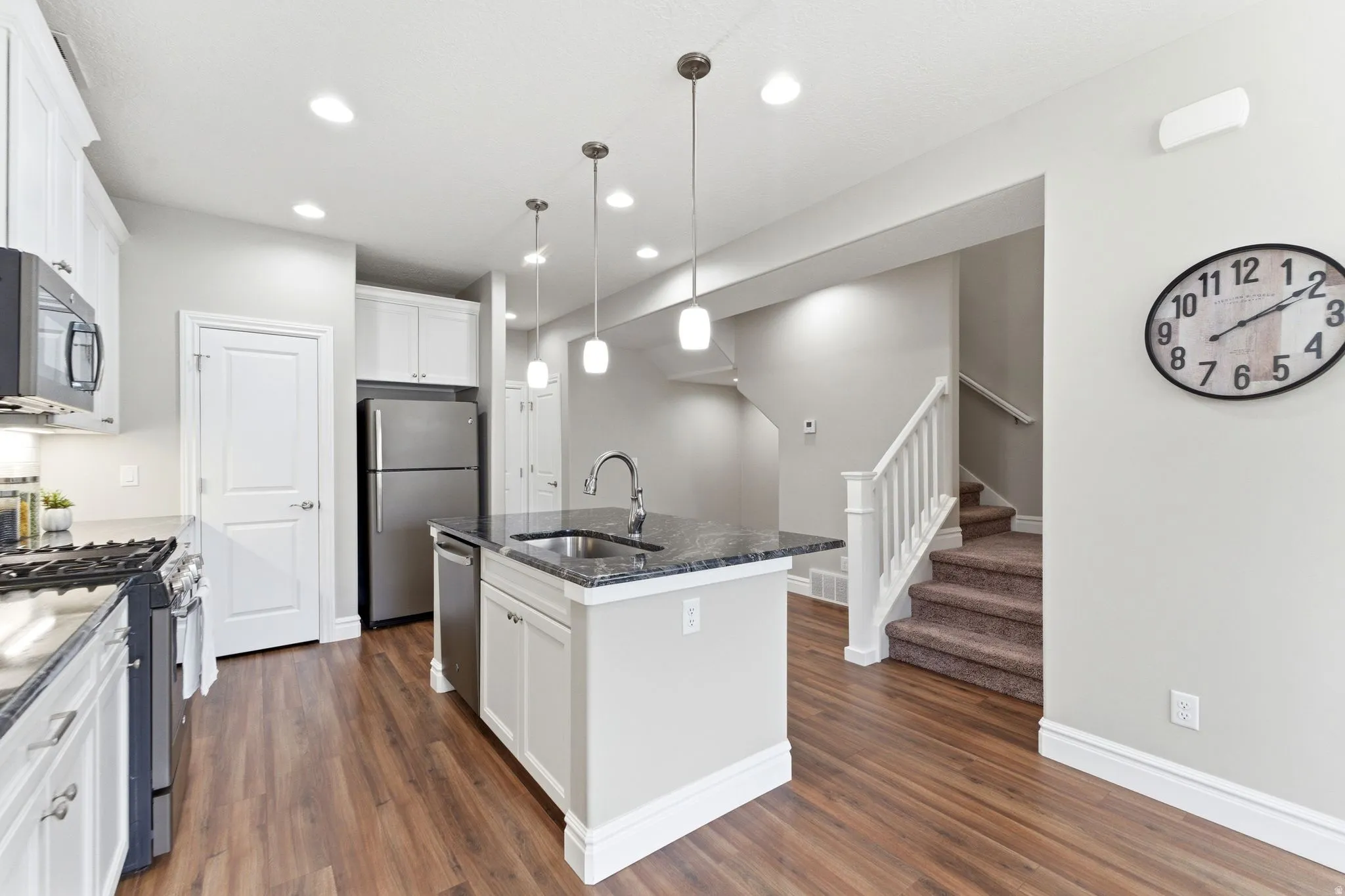 Kitchen featuring wood-finish flooring, white cabinetry, dark countertops, a central island with sink, and stainless steel appliances