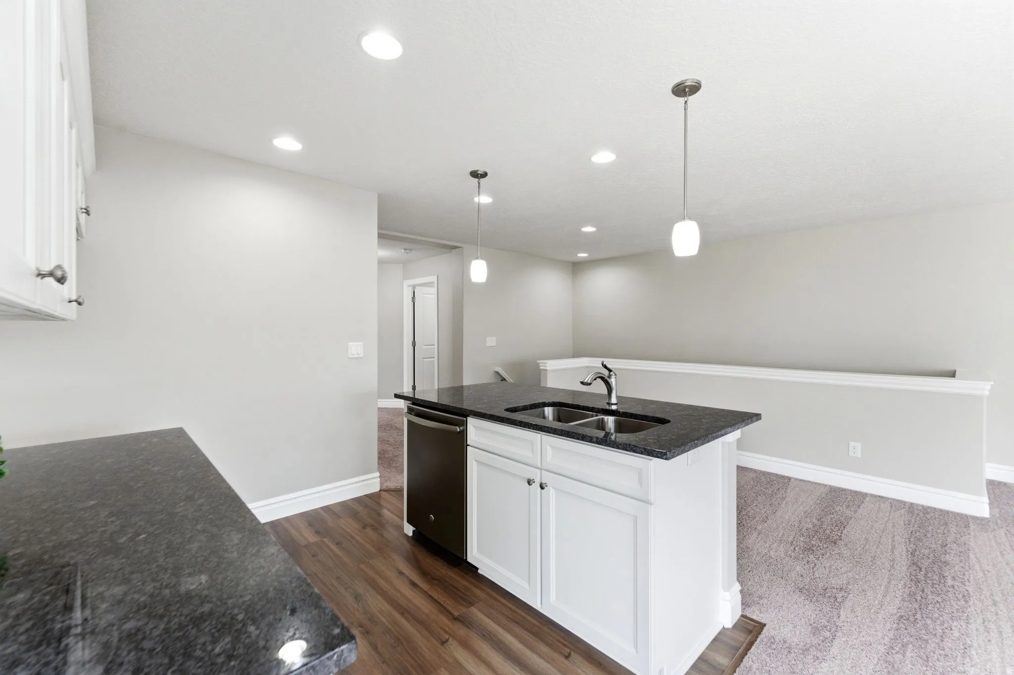 Kitchen island featuring a dual-basin stainless steel sink, a pull-down faucet, and white cabinetry with dark countertops