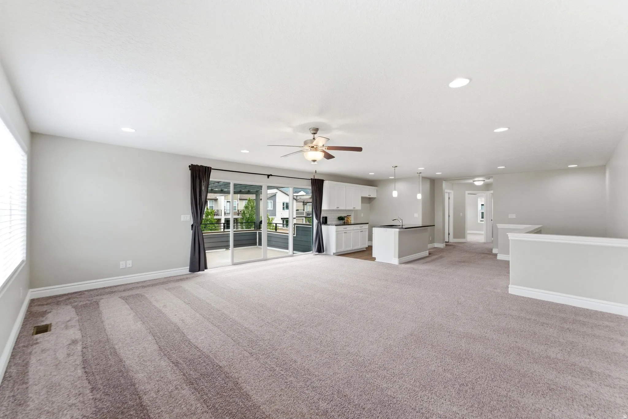 Expansive living area with neutral carpeting, recessed lighting, and a ceiling fan