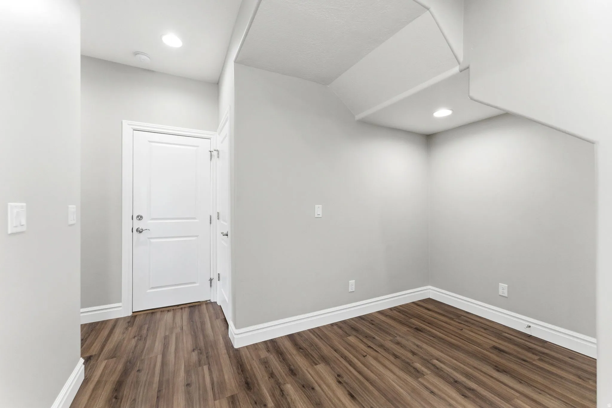 Interior space featuring wood-finish flooring, recessed lighting, and a white two-panel door with brushed nickel hardware