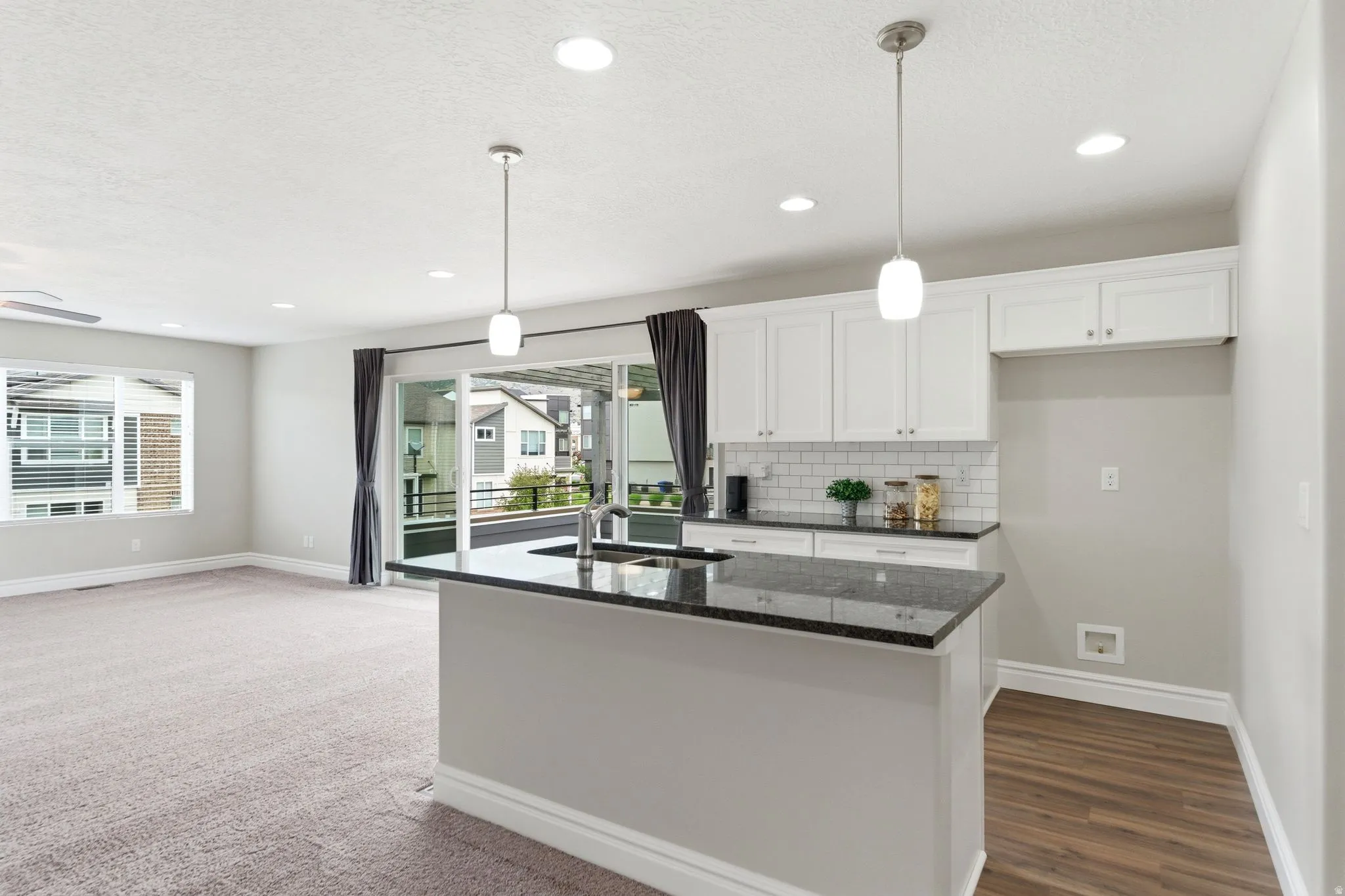 Kitchen island with a dark countertop and undermount sink, complemented by white cabinetry and a subway tile backsplash