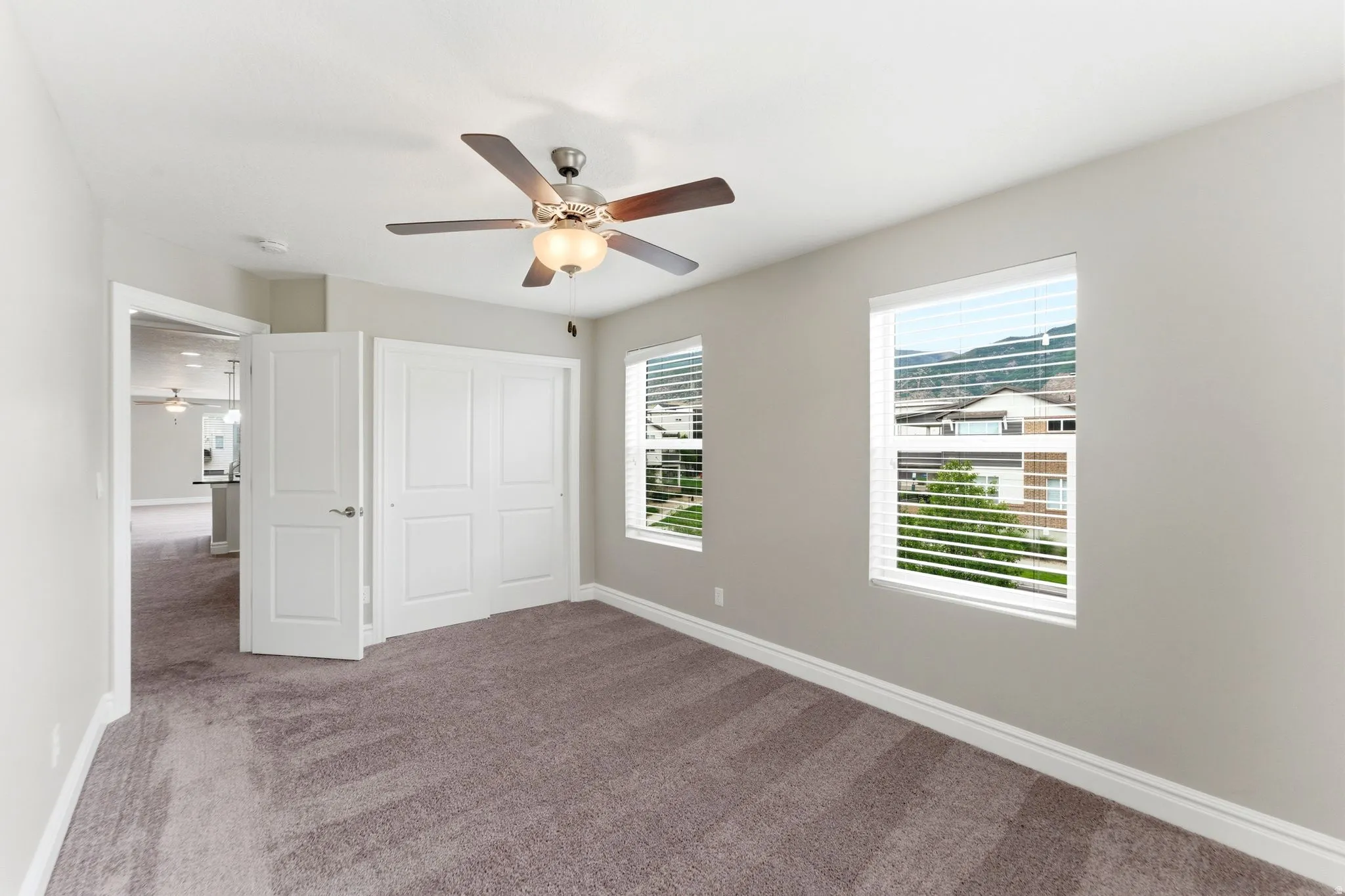 Spacious bedroom featuring neutral wall tones, two windows with blinds, a ceiling fan with light fixture, and plush carpet flooring
