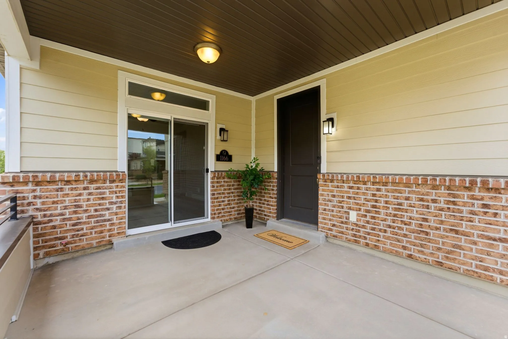 Covered porch with concrete flooring, brick wainscoting, and beige horizontal siding