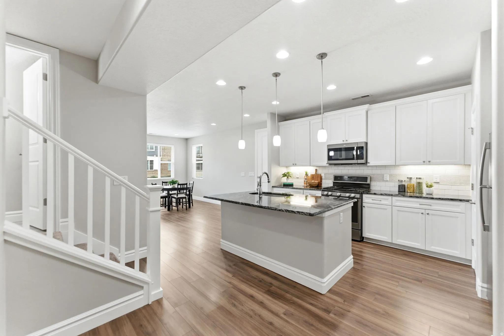 Kitchen featuring an island with a dark countertop, white shaker-style cabinetry, stainless steel appliances, subway tile backsplash, and wood-finish flooring
