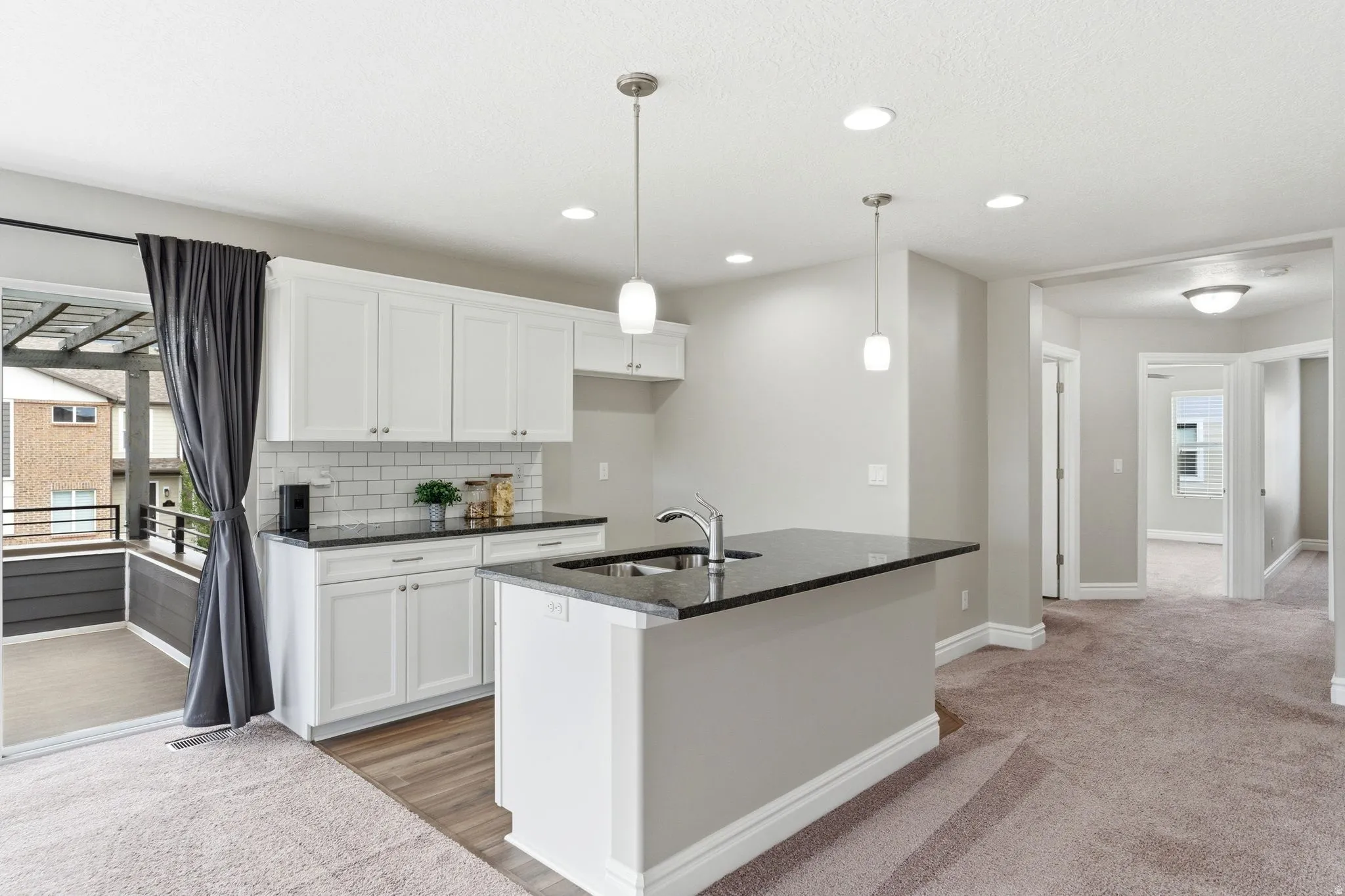 Open concept kitchen featuring white shaker cabinetry, dark countertops, a subway tile backsplash, and a central island with an undermount sink