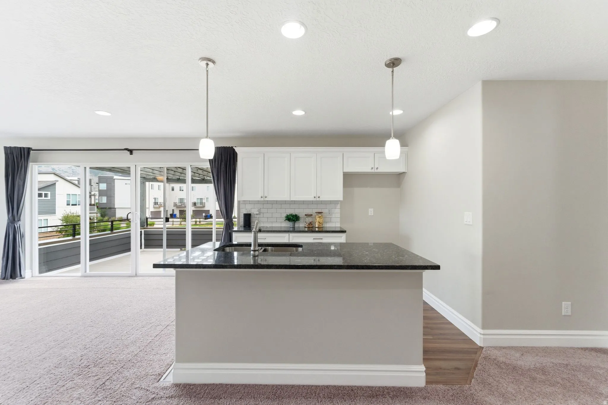 Kitchen island with a dark countertop and integrated sink, complemented by white upper cabinetry and a subway tile backsplash
