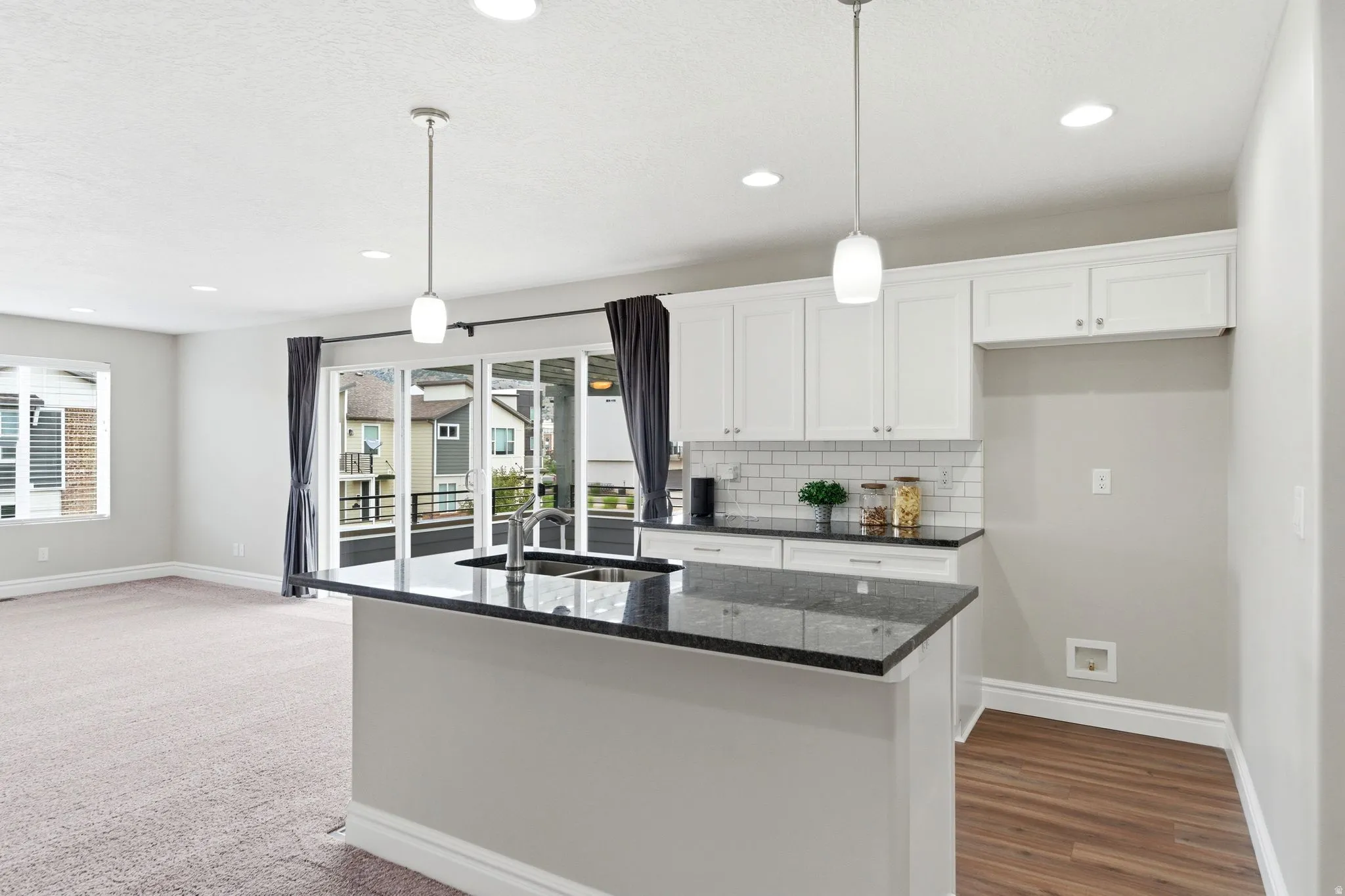 Modern kitchen island with dark countertop, white cabinetry, subway tile backsplash, and recessed lighting