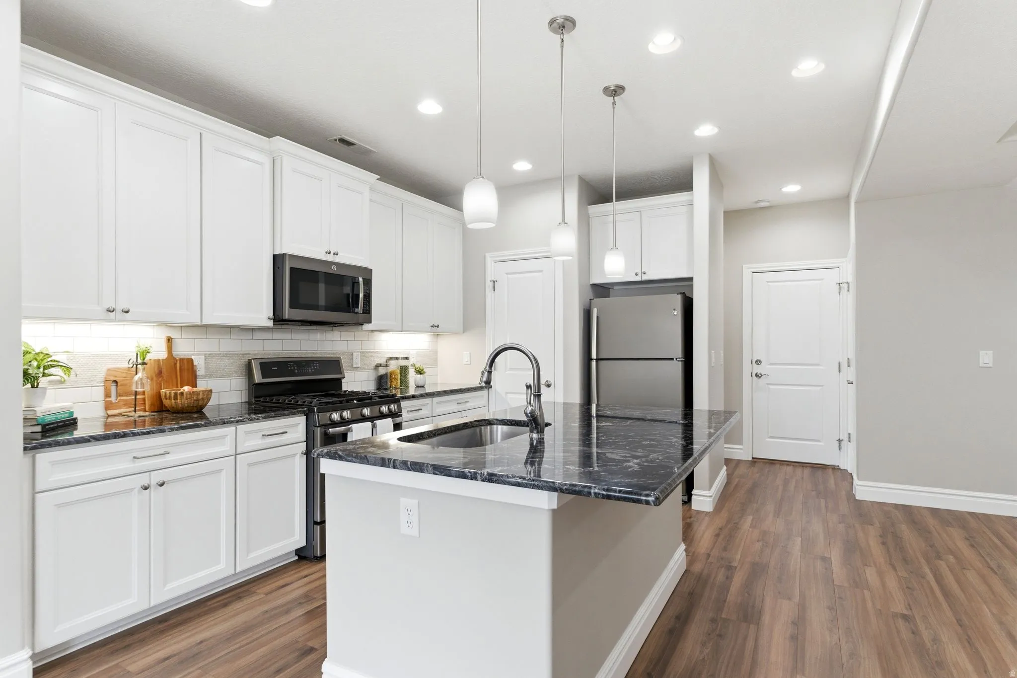 Contemporary kitchen featuring white cabinetry, dark stone countertops, stainless steel appliances, and wood-finish flooring