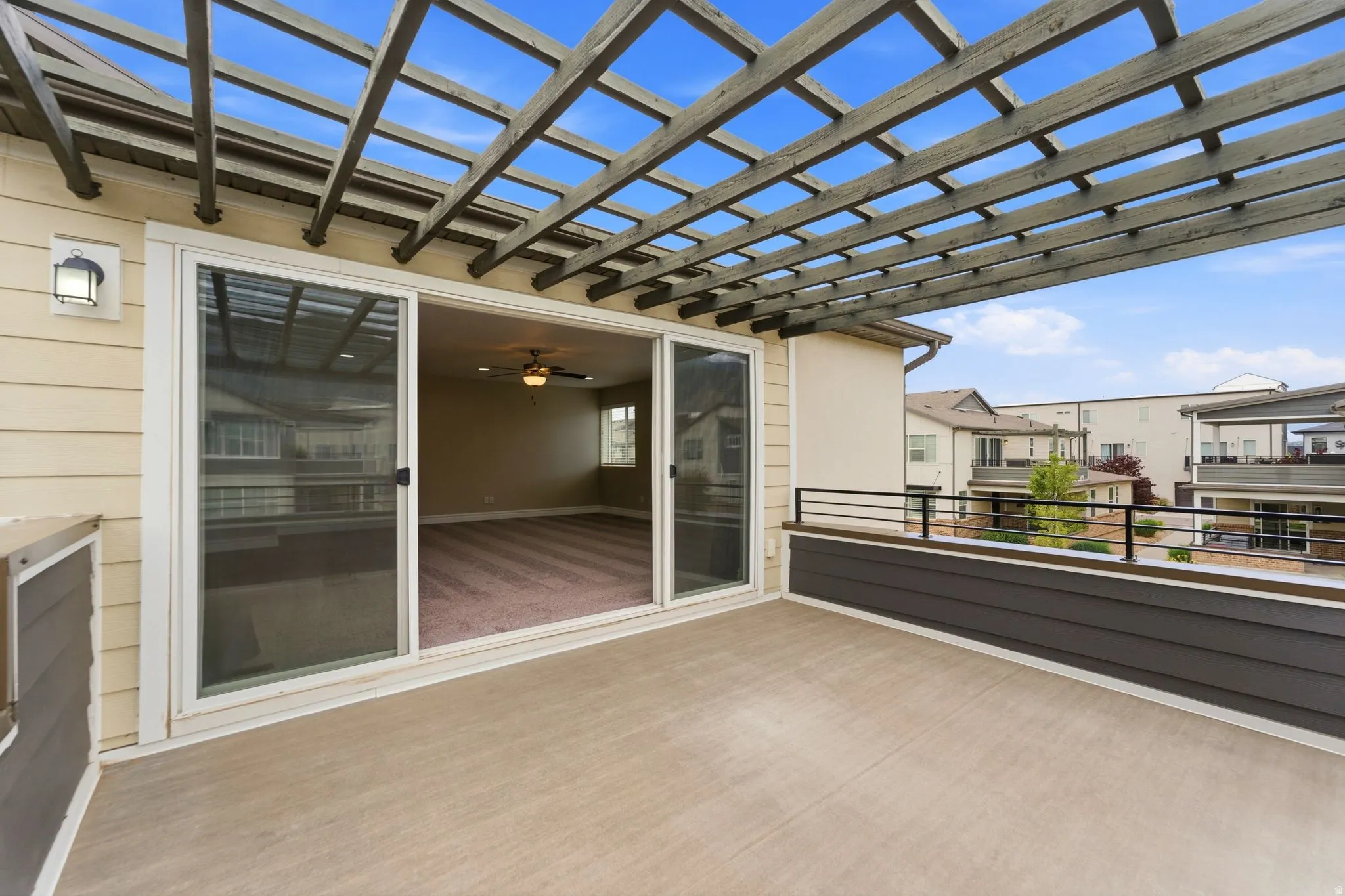 Spacious outdoor patio featuring a wooden pergola, concrete flooring, and an exterior wall lantern
