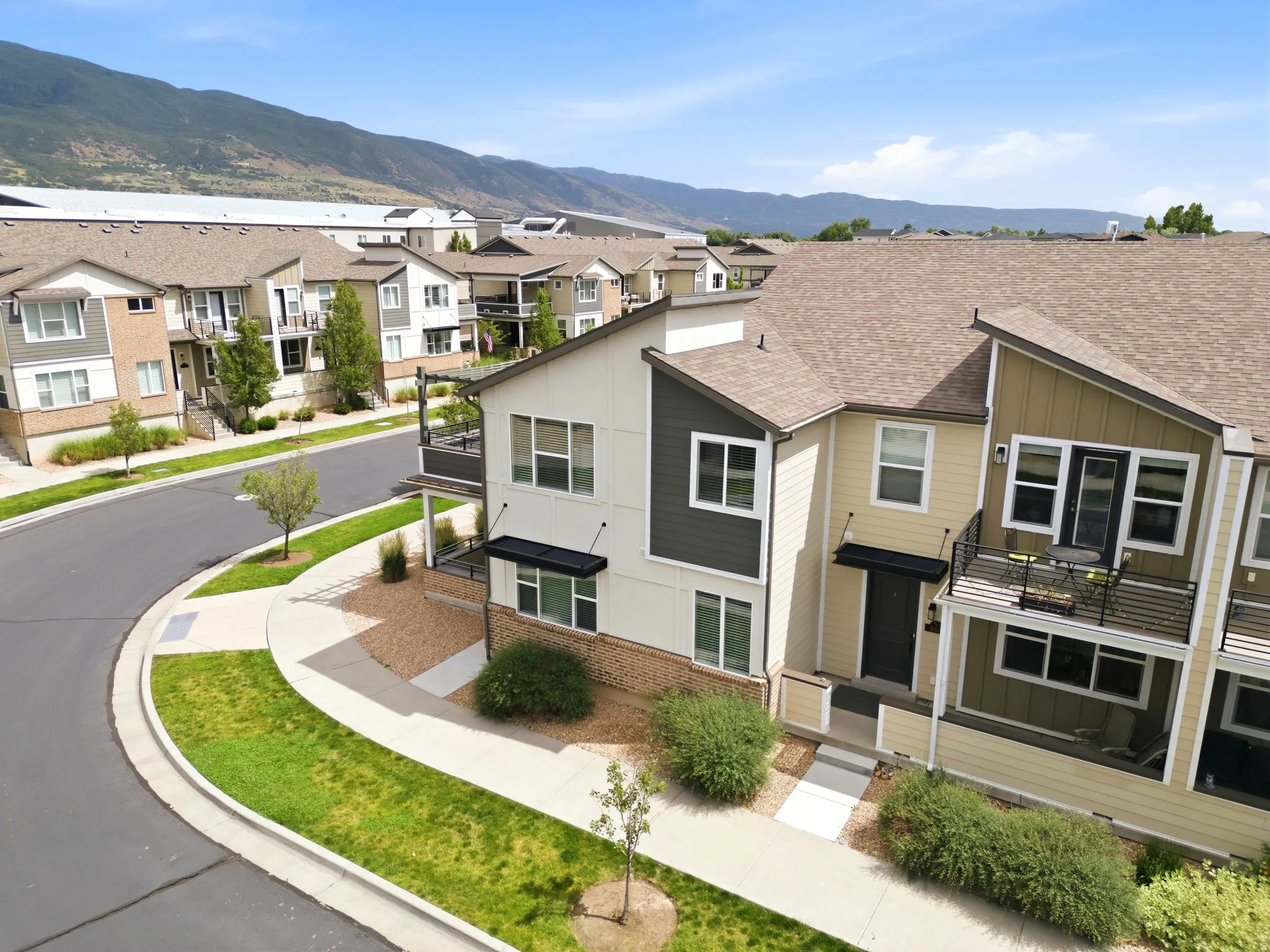 Multi-level townhome featuring a neutral-toned exterior with dark accents, a front porch, and an upper-level balcony